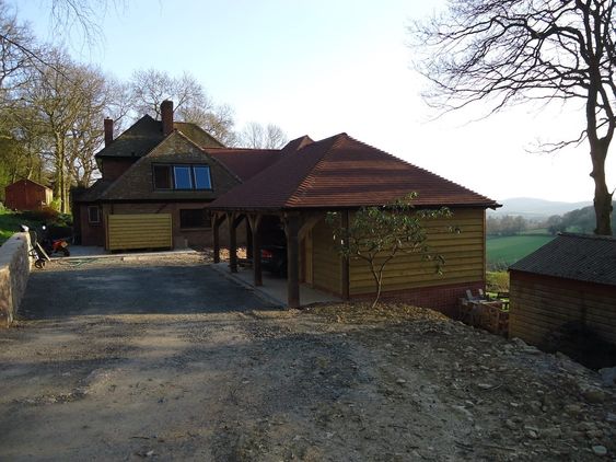 A new timber framed garage with oak pillars and wooden slats overlooking west Malvern Hills