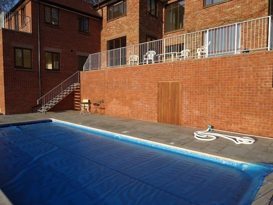A swimming pool set with surrounding slabbing and overlooked by a balcony