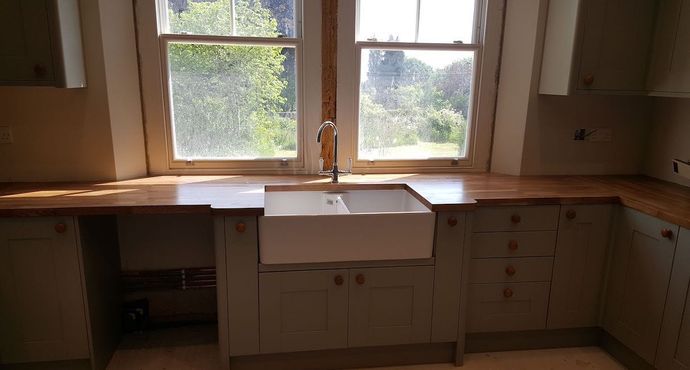 A new kitchen being installed with a belfast sink centered between uPVC windows