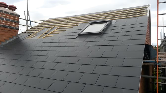 A pitched roof having its slate tiles replaced and two new Velux roof lights being installed.